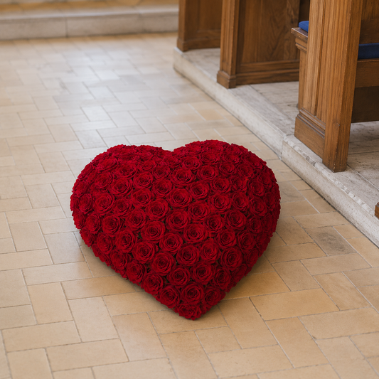 A heart-shaped red rose cushion placed on a light beige tiled floor in front of wooden pews.