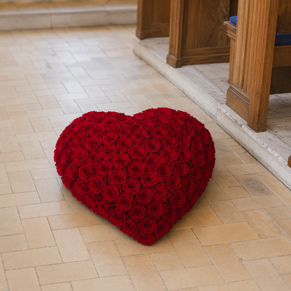 A heart-shaped red rose cushion placed on a light beige tiled floor in front of wooden pews.