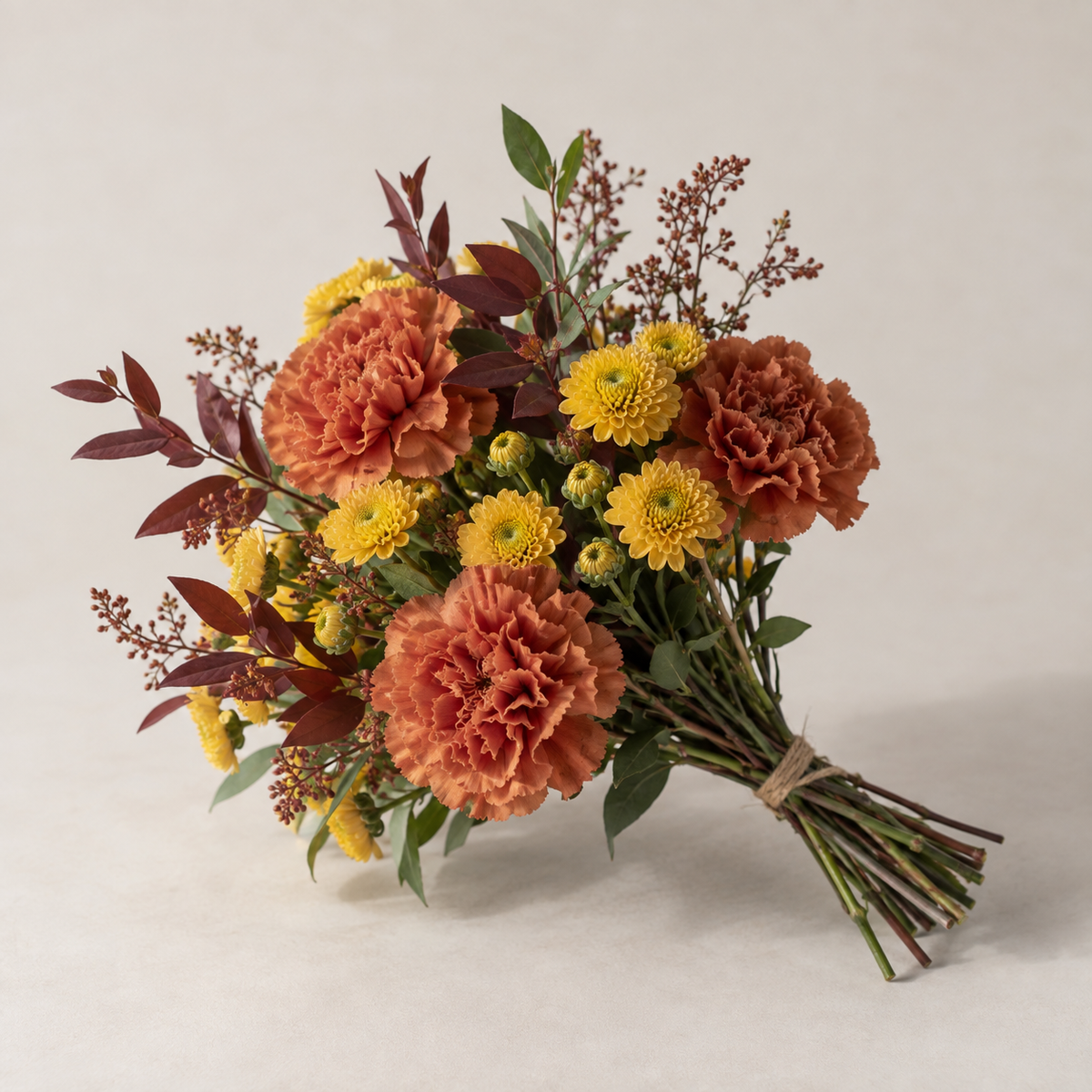 A petite seasonal bouquet in warm autumn colours, with carnations, spray chrysanthemums and foliage.
